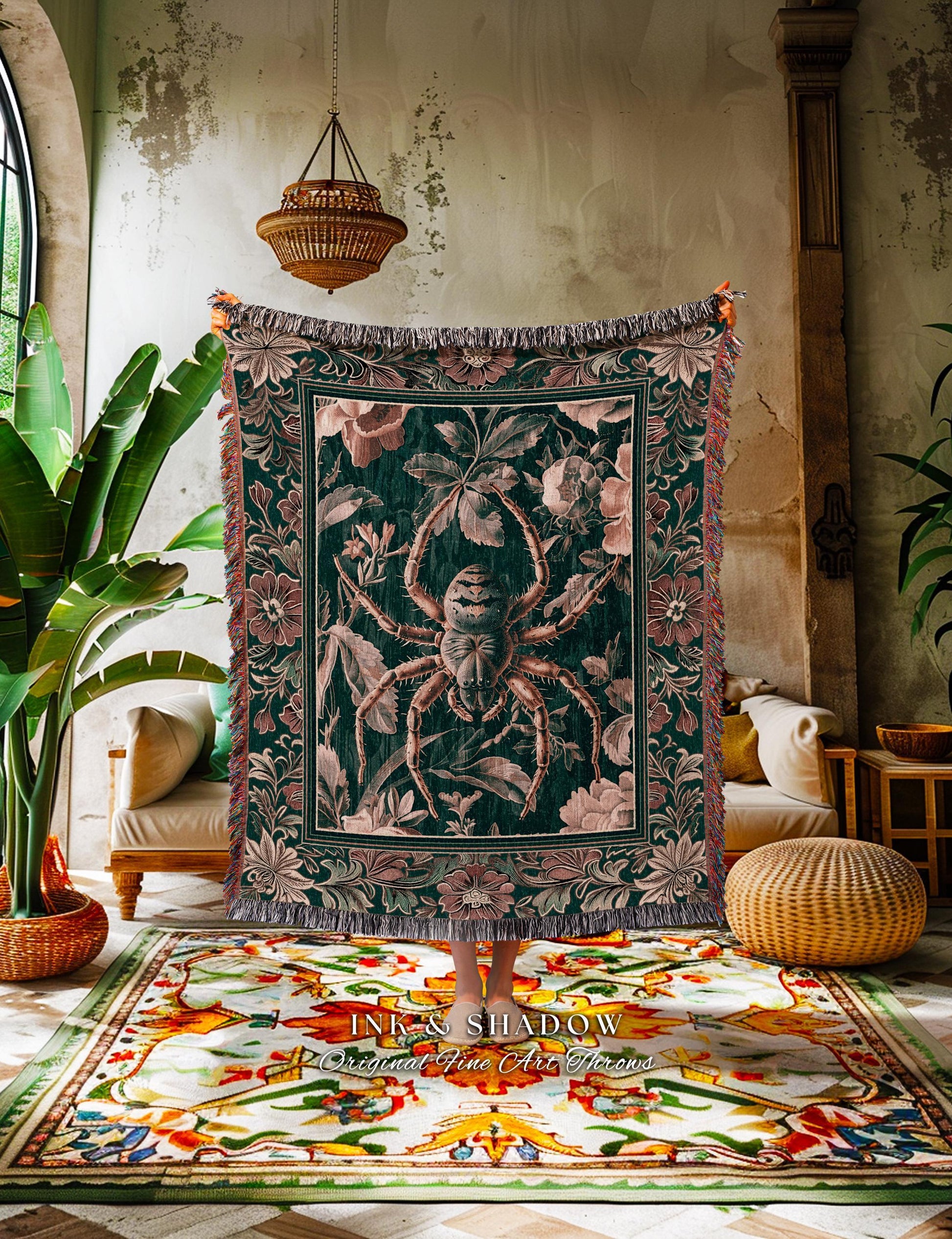 May include: A dark green throw blanket with a large spider design in the center, surrounded by floral patterns in pink and cream. The blanket has a fringed edge and the text "INK & SHADOW Original Fine Art Throws" at the bottom.