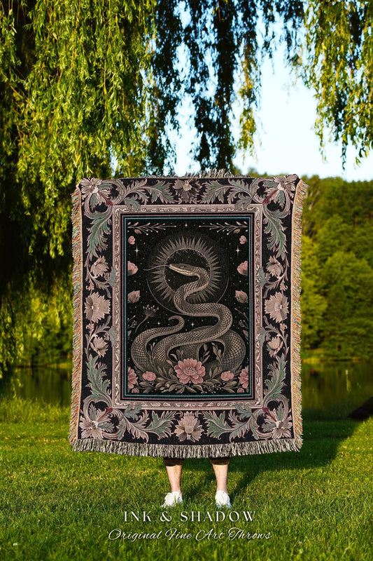 May include: A black throw blanket with a detailed illustration of a snake, flowers, and celestial elements. The blanket has a fringed edge and the text "INK & SHADOW Original Fine Art Throws". The design is in shades of gray, pink, and black.