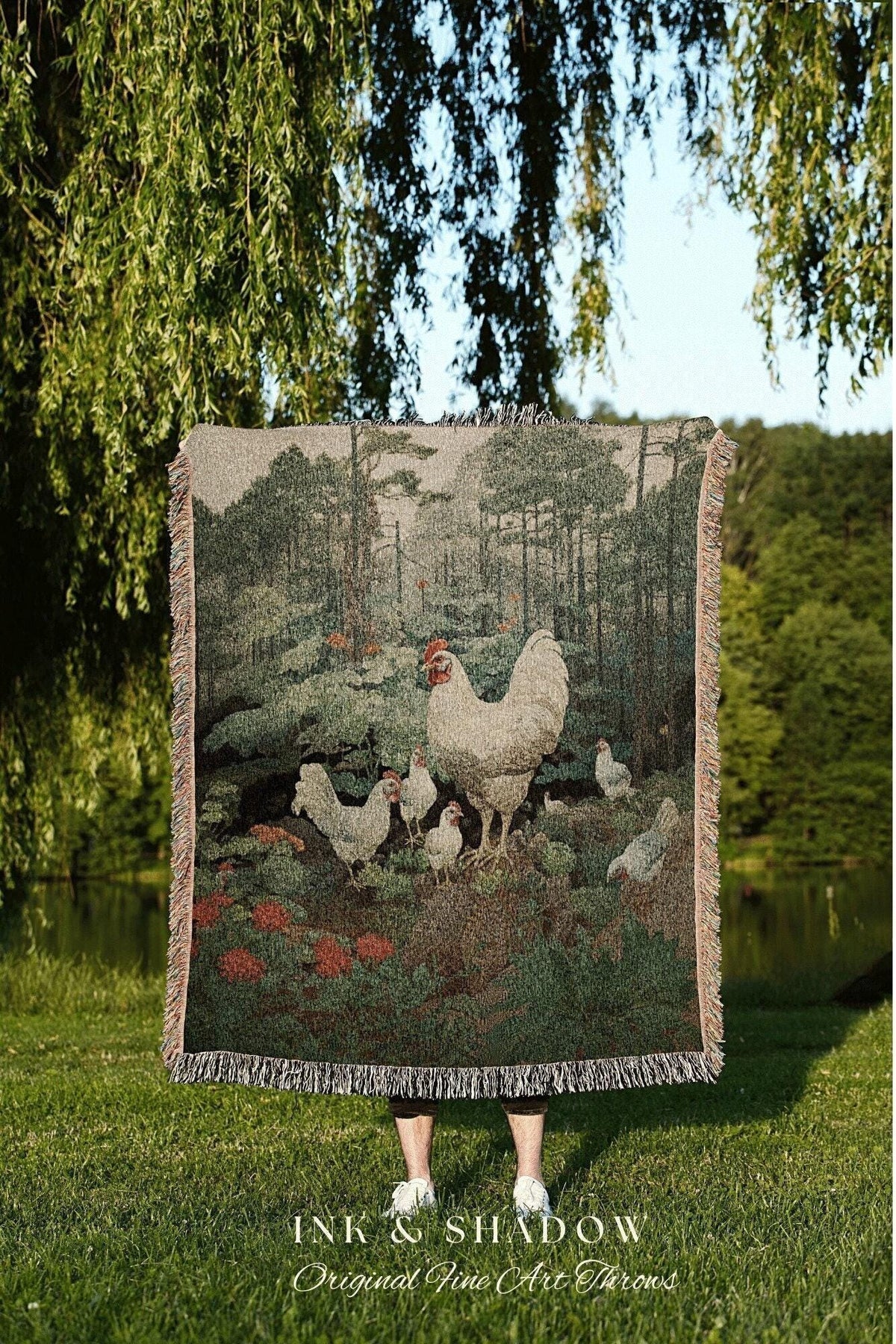 May include: A woven tapestry throw blanket featuring a pastoral scene with chickens and a forest backdrop. The blanket has a fringed edge and is primarily green, brown, and beige. The text "INK & SHADOW Original Fine Art Throws" is at the bottom.