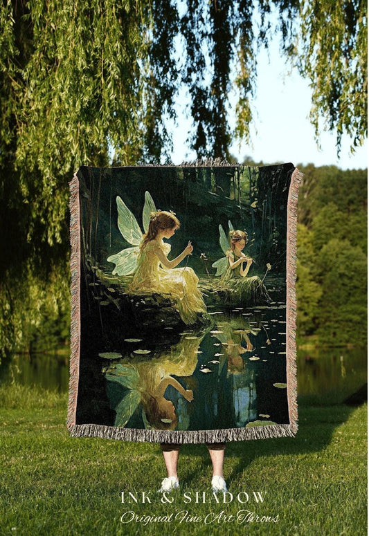 May include: A woven throw blanket featuring a serene scene of two fairies by a pond, with a reflection in the water. The artwork is in shades of green, yellow, and black. The blanket has a fringed edge and the text "INK & SHADOW Original Fine Art Throws".