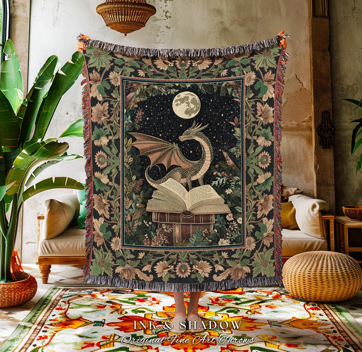 May include: A tapestry throw blanket featuring a dragon perched atop an open book under a full moon. The design is set against a starry night sky and surrounded by floral patterns in shades of green, brown, and cream. The blanket has a fringed edge.