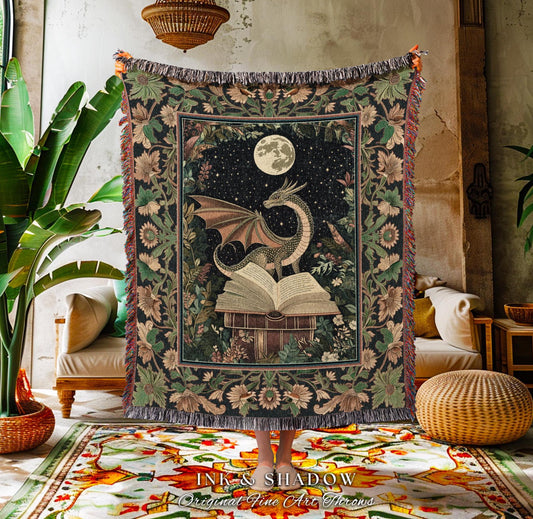 May include: A tapestry throw blanket featuring a dragon perched atop an open book under a full moon. The design is set against a starry night sky and surrounded by floral patterns in shades of green, brown, and cream. The blanket has a fringed edge.