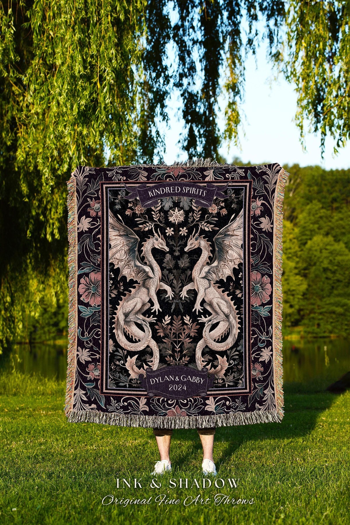 May include: A dark tapestry throw blanket featuring two symmetrical dragons with outstretched wings. The blanket has a floral border and the words "Kindred Spirits" and "Dylan & Gabby 2024" are displayed. The words "INK & SHADOW Original Fine Art Throws" are at the bottom.