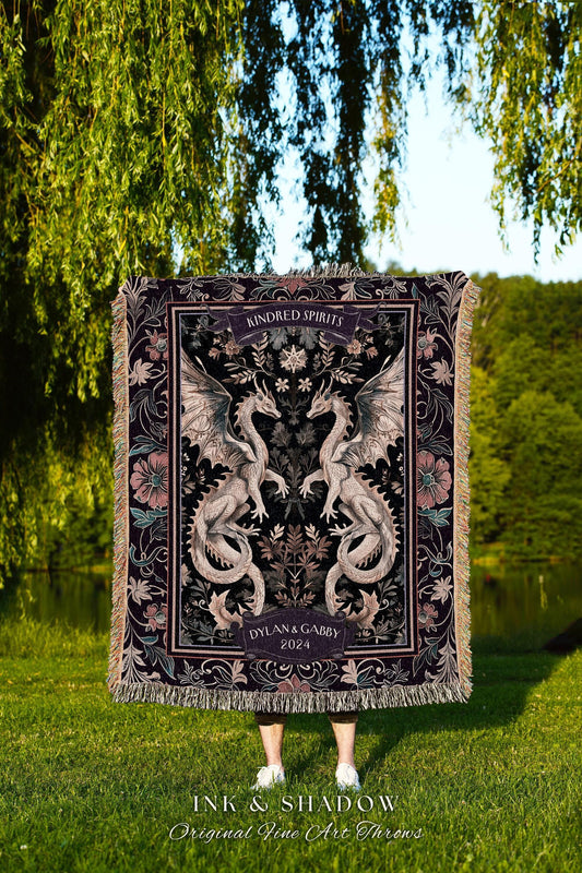 May include: A dark tapestry throw blanket featuring two symmetrical dragons with outstretched wings. The blanket has a floral border and the words "Kindred Spirits" and "Dylan & Gabby 2024" are displayed. The words "INK & SHADOW Original Fine Art Throws" are at the bottom.