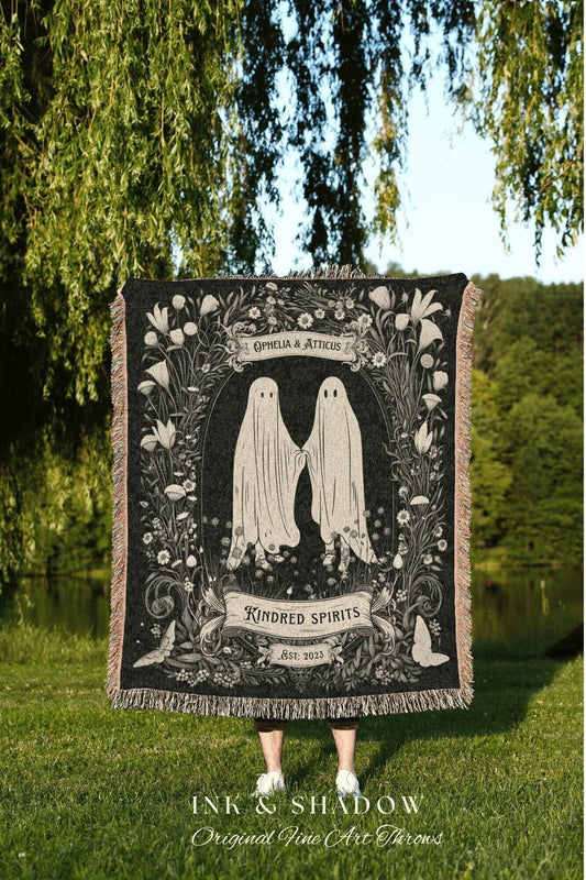 May include: Black throw blanket featuring two ghost figures holding hands, surrounded by floral designs. The words "Kindred Spirits" and "Ophelia & Atticus" are displayed. The blanket has a fringed edge and the text "INK & SHADOW Original Fine Art Throws".