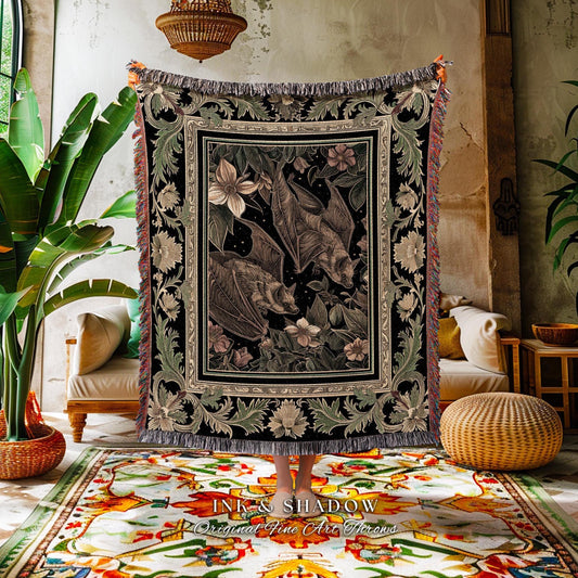 May include: A black and beige woven throw blanket featuring a detailed illustration of bats, flowers, and foliage. The blanket has a decorative border and fringe. The text "INK & SHADOW Original Fine Art Throws" is visible at the bottom.