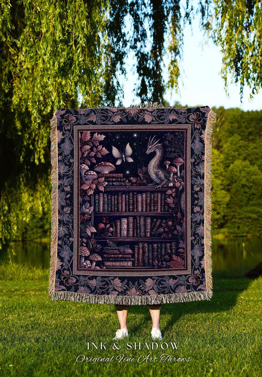 May include: A tapestry throw blanket featuring a fantasy scene with a dragon, butterfly, and mushrooms in front of a bookshelf. The throw has a dark background with a decorative border and fringe. The text "INK & SHADOW Original Fine Art Throws" is at the bottom.
