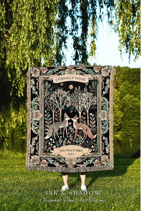 May include: A black tapestry throw blanket with a forest scene featuring two foxes, trees, and floral elements. The blanket has a fringed edge and the text "Eternally Yours" and "Dylan & Gabby 2024". The blanket is displayed outdoors.