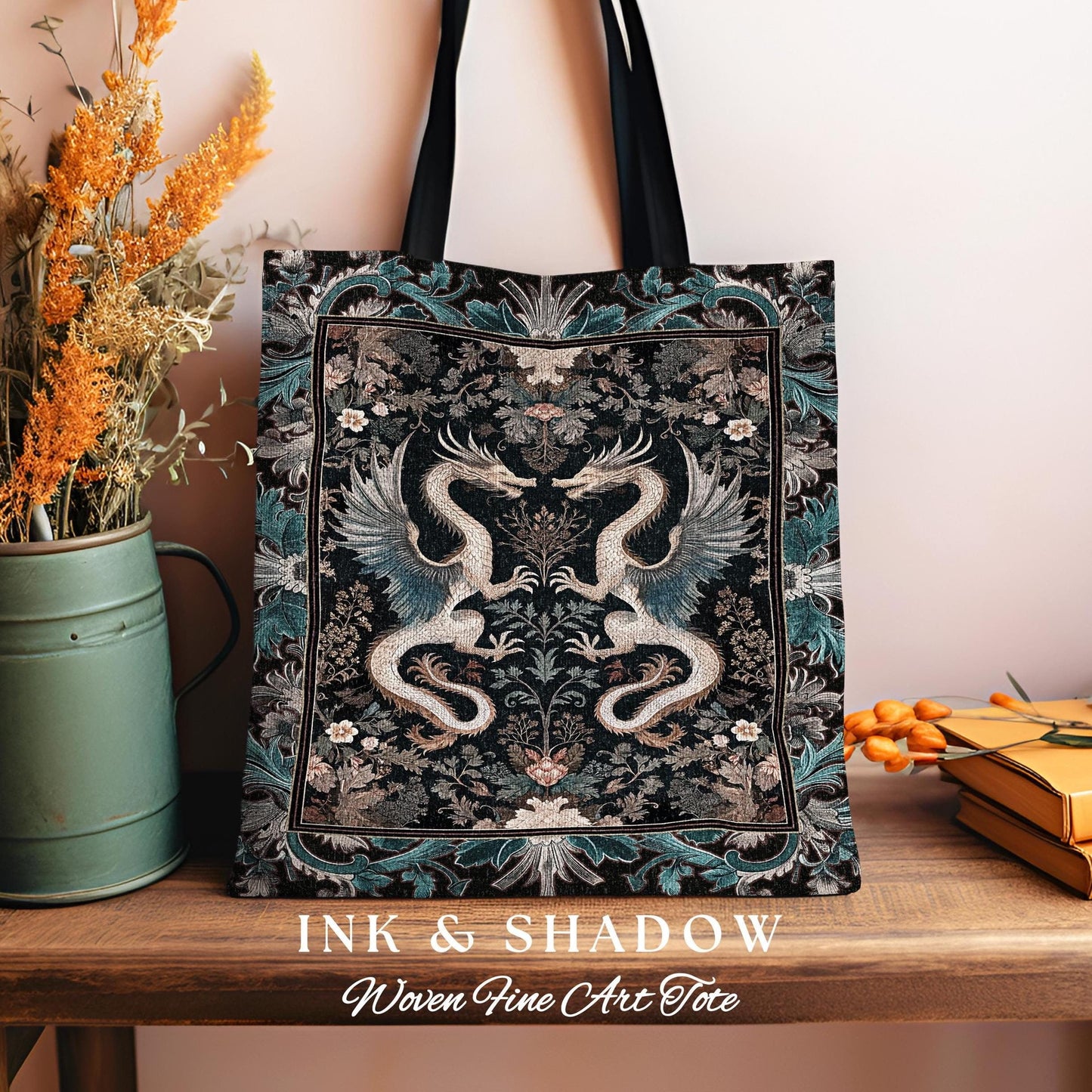 May include: A black canvas tote bag with a woven tapestry design featuring two dragons in a floral pattern. The bag has black straps and the text "INK & SHADOW Woven Fine Art Tote" printed on the bottom.