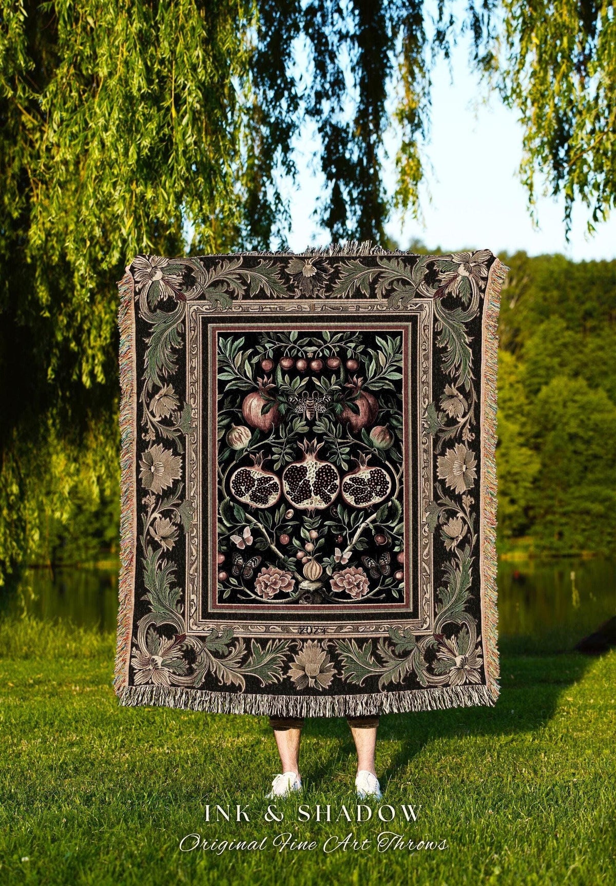 May include: A decorative throw blanket with a detailed pomegranate design in shades of black, green, and pink. The blanket has a fringed edge and features the text "INK & SHADOW Original Fine Art Throws".