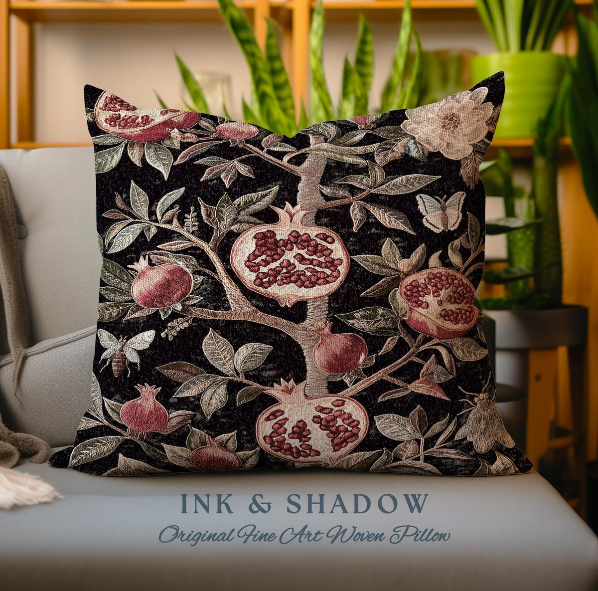 May include: A decorative pillow with a woven design of a pomegranate tree with red pomegranates, green leaves, and a butterfly. The pillow has a black background and the text "INK & SHADOW Original Fine Art Woven Pillow" is printed on the bottom.