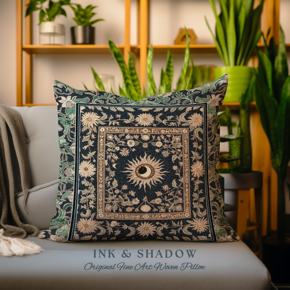 May include: A decorative throw pillow with a dark blue background and a gold and green floral pattern. The center of the pillow features a sun and moon design with a gold frame. The pillow has the text "INK & SHADOW Original Fine Art Woven Pillow" printed on the bottom.