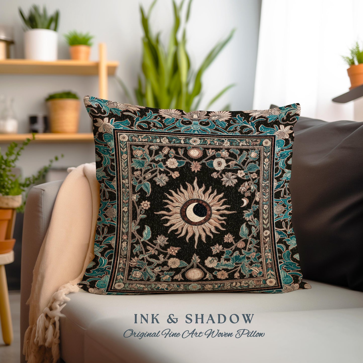 May include: A decorative throw pillow with a black background and a teal border. The pillow features a woven design of a sun and moon with floral accents. The text "INK & SHADOW Original Fine Art Woven Pillow" is printed below the pillow.