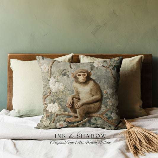 May include: A square throw pillow featuring a woven tapestry design of a brown monkey perched on a tree branch surrounded by white flowers and green foliage. The text INK & SHADOW Original Fine Art Woven Pillow is printed at the bottom center.