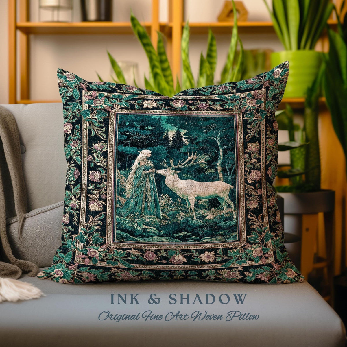 May include: A decorative pillow with a woven tapestry design featuring a woman in a forest with a white deer. The pillow has a black background with green and pink floral accents. The text "INK & SHADOW Original Fine Art Woven Pillow" is printed below the pillow.