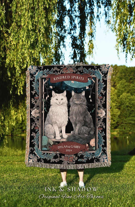 May include: A black throw blanket featuring a framed illustration of two cats, one white and one gray, with the text "Kindred Spirits" and "Dylan & Gabby 2024." The blanket has a decorative border and fringe.