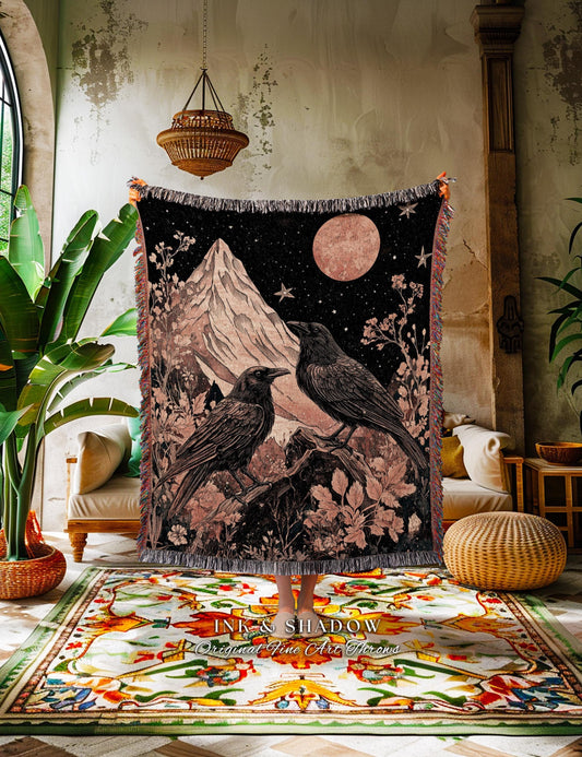 May include: Black woven throw blanket featuring a mountain scene with two crows perched on a branch under a starry night sky and a large pink moon. The blanket has a fringed edge and the text "INK & SHADOW Original Fine Art Throws".