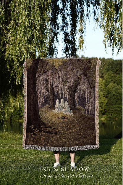 May include: A woven throw blanket featuring a forest scene with three ghostly figures. The blanket has a brown and green color palette with a fringed edge. The text "INK & SHADOW Original Fine Art Throws" is at the bottom.
