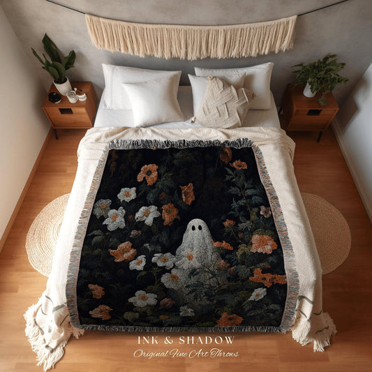 May include: A black throw blanket with a floral and ghost design. The blanket features white, orange, and green flowers, with a white ghost in the center. The text "INK & SHADOW Original Fine Art Throws" is at the bottom.