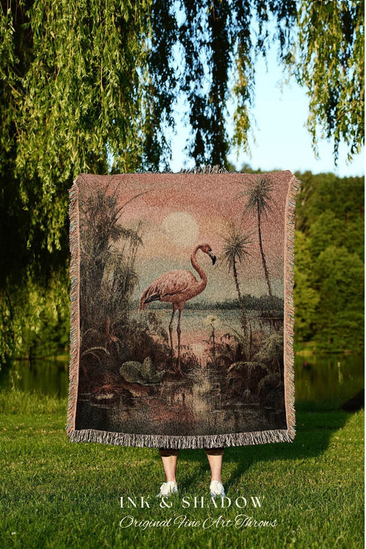 May include: A woven throw blanket featuring a flamingo in a tropical landscape with palm trees and a sunset. The blanket has a fringed edge and the text "INK & SHADOW Original Fine Art Throws" at the bottom.