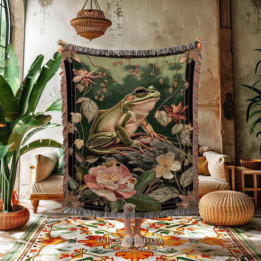 May include: A woven tapestry featuring a large green frog on a rock, surrounded by flowers and foliage. The tapestry has a dark green background and a fringed edge. The text "INK & SHADOW Original Fine Art Throws" is at the bottom.