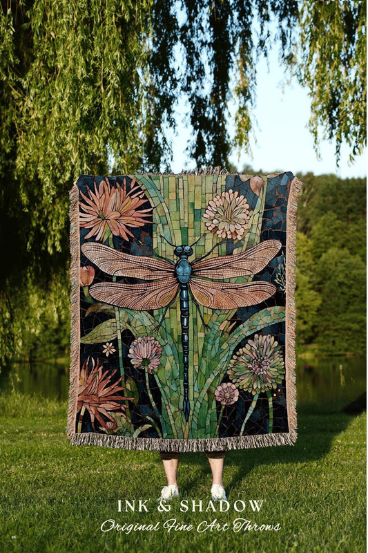 May include: A decorative throw blanket featuring a large dragonfly design with a mosaic-style background. The dragonfly has brown wings and a blue body, surrounded by flowers in shades of pink and green. The blanket has a fringed edge and the text "INK & SHADOW Original Fine Art Throws".