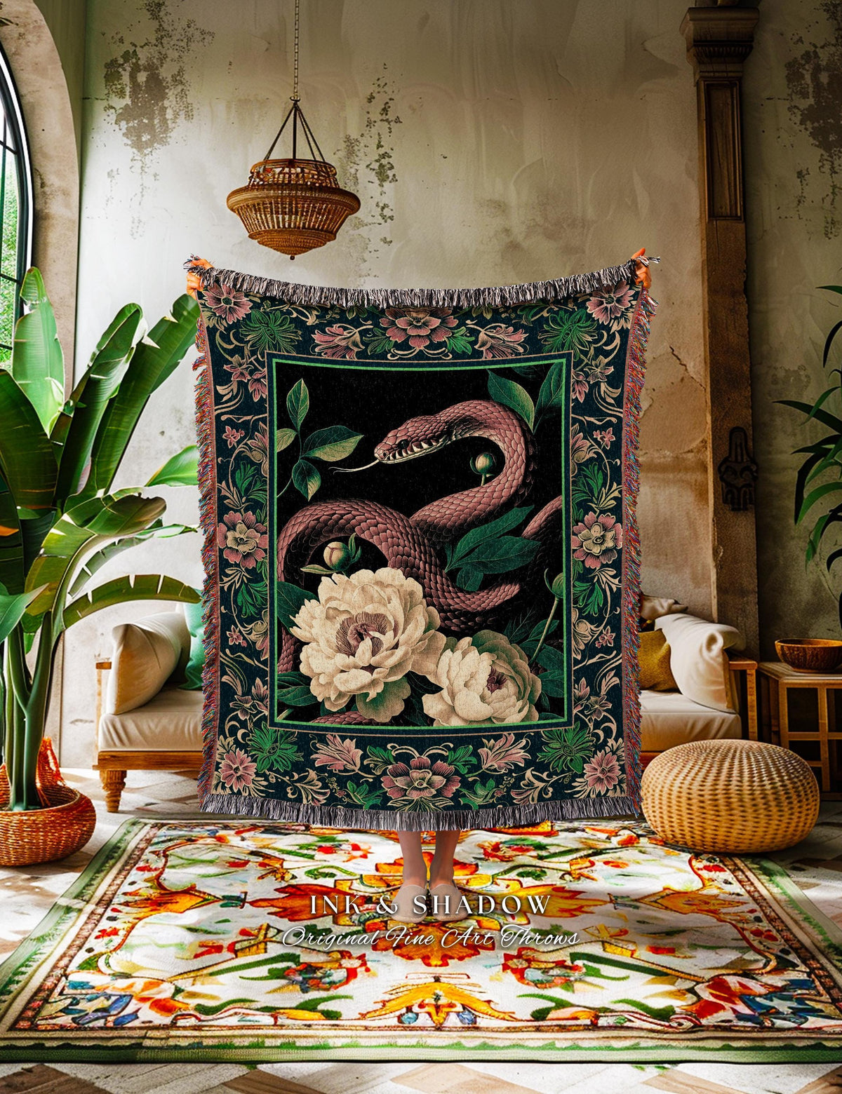 May include: A dark green and black tapestry throw blanket featuring a pink snake, white peonies, and green foliage. The blanket has a floral border with pink flowers and a fringed edge. The text "INK & SHADOW Original Fine Art Throws" is visible.