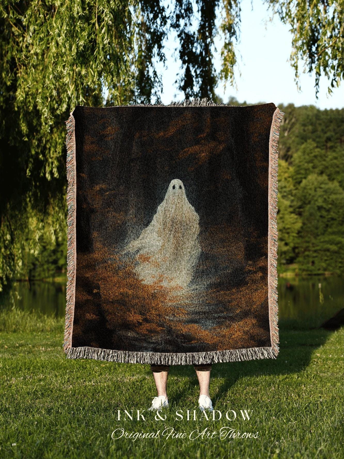 May include: A woven throw blanket featuring a ghostly figure against a dark, textured background. The blanket has a fringed edge and the text "INK & SHADOW Original Fine Art Throws" at the bottom. The color palette includes black, brown, and white.