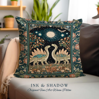 May include: A woven pillow with a dark green background and a floral pattern. The center of the pillow features a scene of two dinosaurs with a full moon and stars in the background. The text "INK & SHADOW Original Fine Art Woven Pillow" is printed below the image.