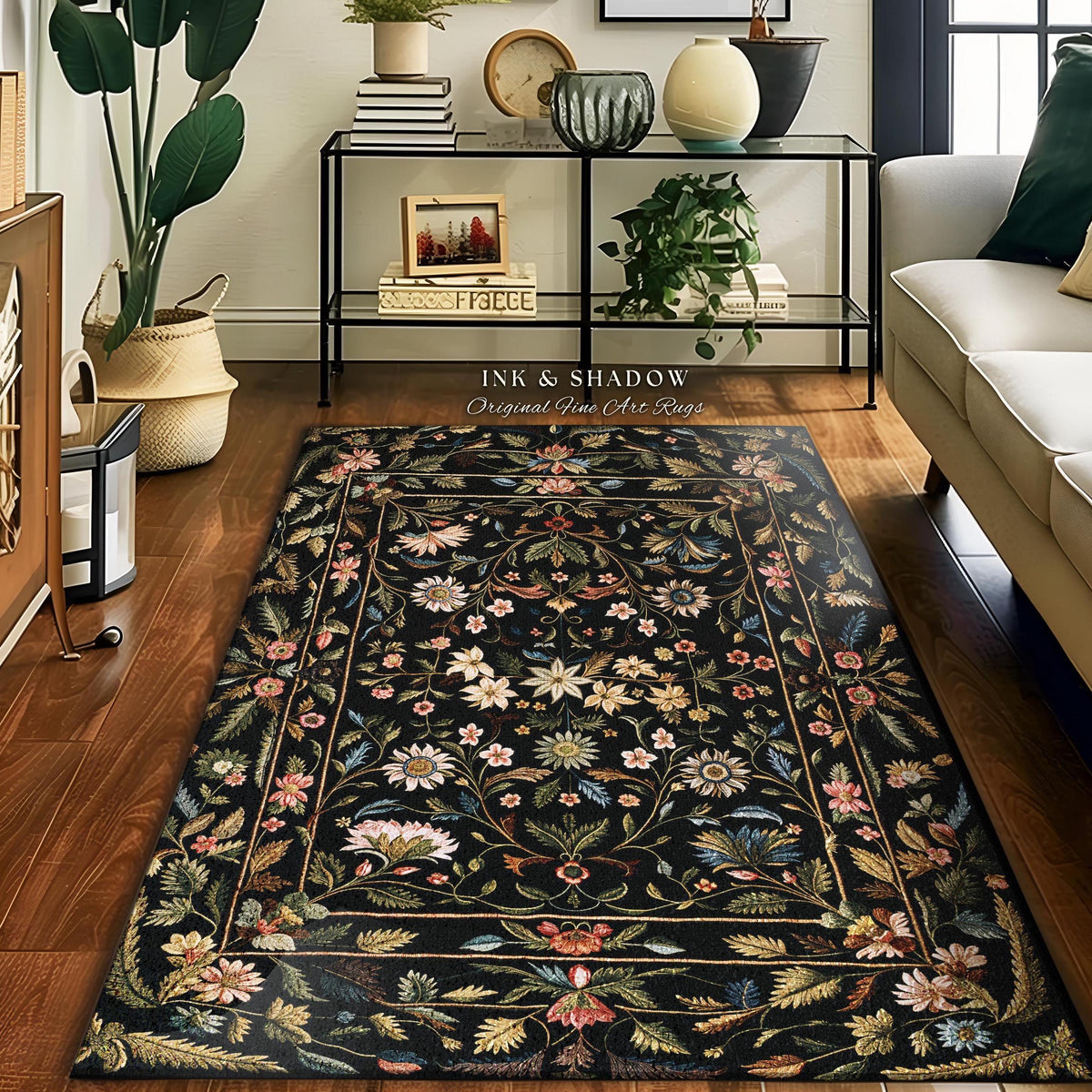 May include: A rectangular black rug with a floral design. The rug features a border and is adorned with flowers in shades of pink, white, and blue. The text "INK & SHADOW Original Fine Art Rugs" is visible.
