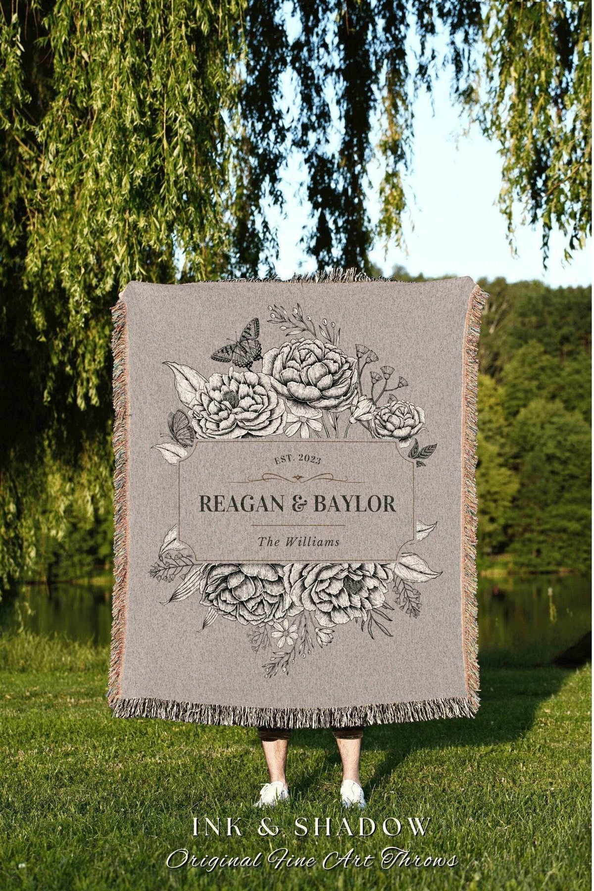 May include: A gray throw blanket with a floral design and the names "REAGAN & BAYLOR" and "The Williams" printed on it. The blanket has a fringed edge and the text "INK & SHADOW Original Fine Art Throws".