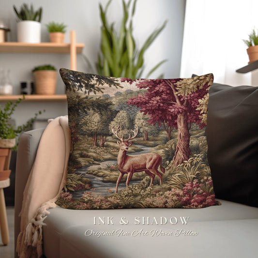 May include: Square decorative pillow featuring a detailed forest scene with a deer standing near a stream. The pillow has a woven texture and includes the text "INK & SHADOW Original Fine Art Woven Pillow". The color palette includes greens, browns, and burgundy.