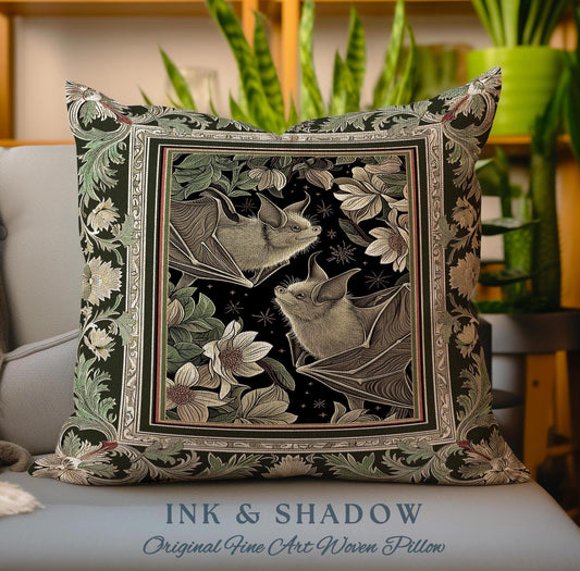 May include: A decorative pillow with a dark green background and a black frame. The frame contains a black and white illustration of two bats with floral details. The text "INK & SHADOW Original Fine Art Woven Pillow" is printed at the bottom of the pillow.