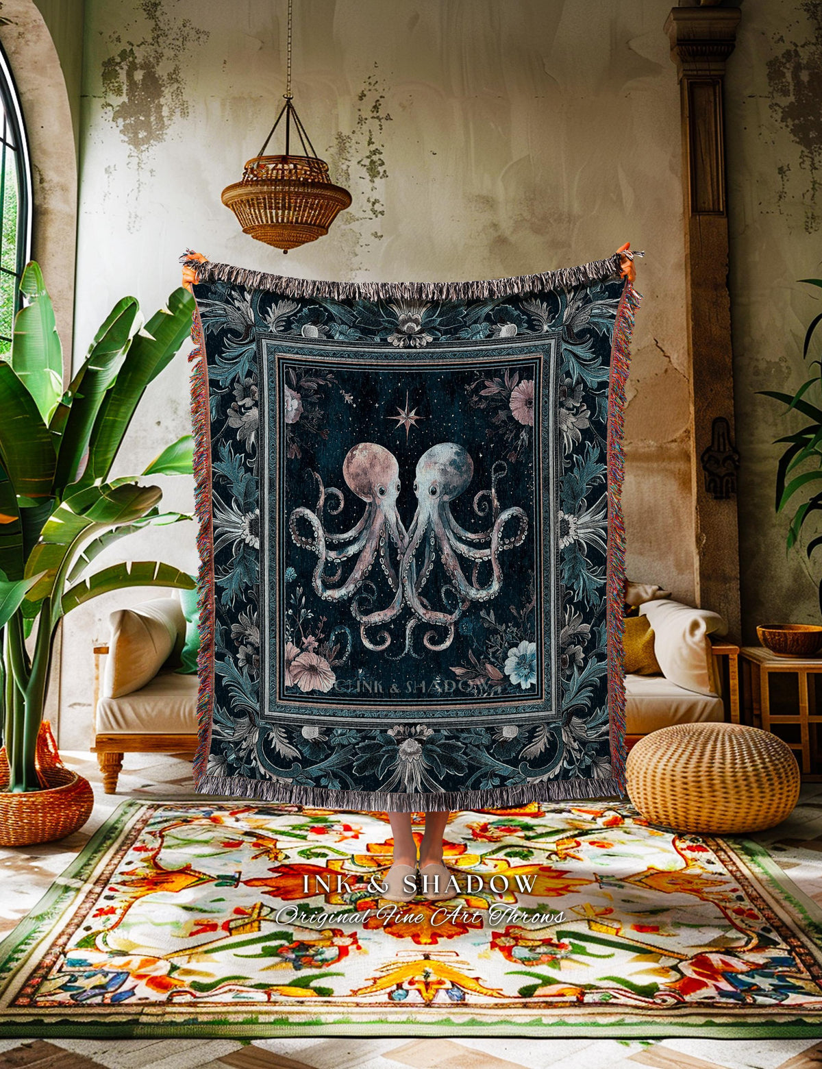 May include: Dark blue throw blanket with a central design of two octopuses, a star, and the text "INK & SHADOW". The blanket has a floral border and fringed edges. The throw is displayed indoors.