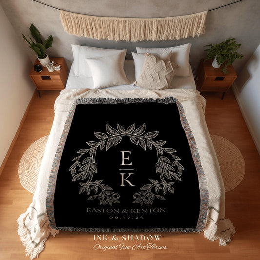 May include: Black throw blanket with a cream-colored leaf wreath design, featuring the initials "E" and "K" and the date "09.17.24". The blanket has a fringed edge and is displayed on a bed with white bedding.